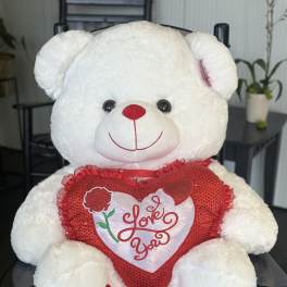 White teddy bear holding a red heart pillow with "Love You" text