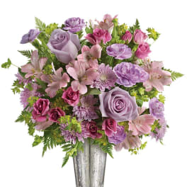 Lavender and pink roses, alstroemeria, carnations, and mums arranged in a tall silver vase