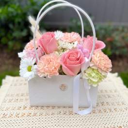 Pink roses and pastel flowers arranged in a white basket with ribbon