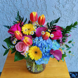 Colorful bouquet of tulips, roses, gerbera daisies, hydrangeas, and small daisies in a glass vase