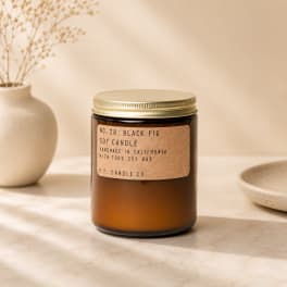 Amber glass candle jar with a gold lid and label on a neutral surface