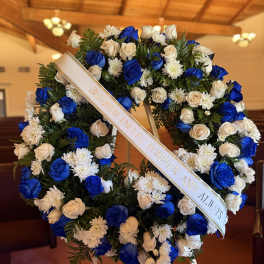 Blue and white floral funeral wreath with a memorial ribbon on an easel