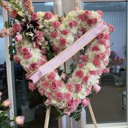 Heart-shaped pink and white floral standing spray with a ribbon across it