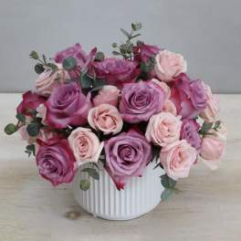 Pink and lavender roses arranged in a white ribbed vase