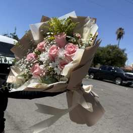Handheld bouquet of pink roses and white flowers wrapped in beige paper