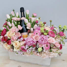 Pink floral arrangement with a champagne bottle in a white box