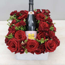 Red roses arranged around a champagne bottle in a white box