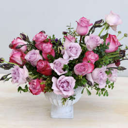 Pink and lavender roses arranged in a white pedestal vase