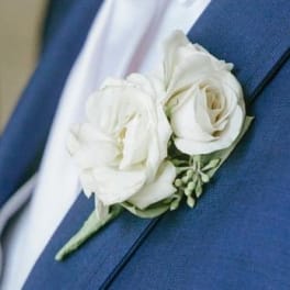 White rose boutonniere pinned to a blue suit jacket