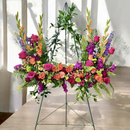 Bright pink, orange, and purple standing floral spray on a metal easel with ferns and trailing foliage