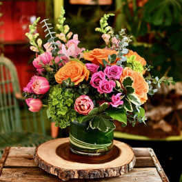 Mixed bouquet of pink and orange flowers in a green glass vase