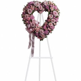 Heart-shaped pink floral wreath on a white easel with ribbon