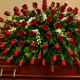 Red rose casket spray with white orchids arranged over a polished wood casket