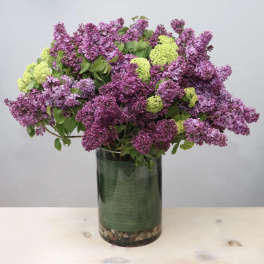 Purple lilac arrangement in a tall glass vase with green accents