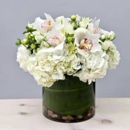 White hydrangeas and orchids in a green glass vase