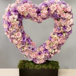 Heart-shaped floral arrangement in pink and purple roses on a moss base