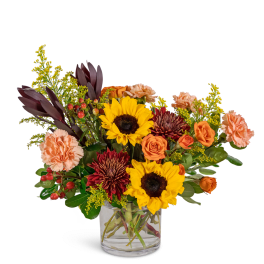 Mixed bouquet of sunflowers, roses, and carnations in a clear glass vase