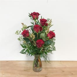 Red roses arranged in a clear glass vase with greenery