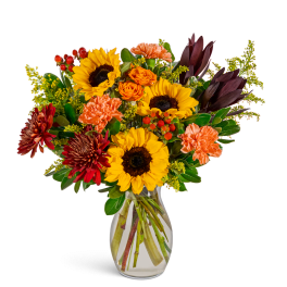 Bouquet of sunflowers, orange roses, and carnations in a clear glass vase