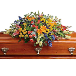Colorful floral casket spray with mixed blooms on a wooden coffin
