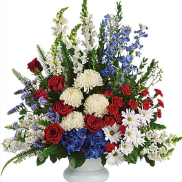 Mixed red, white, and blue floral arrangement in a white pedestal vase