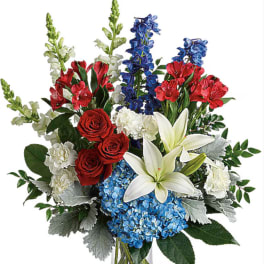 Mixed bouquet of red roses, white lilies, blue hydrangeas, and red blooms in a glass vase