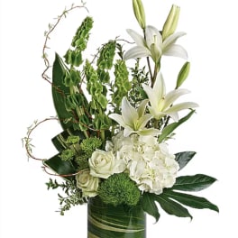 White lilies and roses arranged in a tall green glass vase