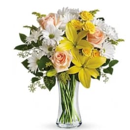 Bouquet of yellow lilies, white daisies, and peach roses in a clear glass vase
