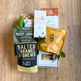 Assorted snack gift box with packaged sweets, jerky, and nuts on a wooden surface.