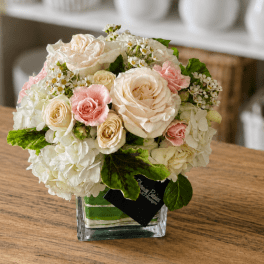 Compact bouquet of cream and pink roses in a clear square vase