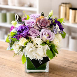 Lavender and white floral arrangement in a clear square vase