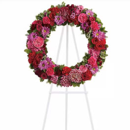 Circular floral wreath on a white easel with red, pink, and purple blooms