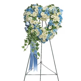 Heart-shaped floral wreath on a stand with blue and white flowers and a ribbon