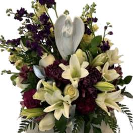 White lilies and purple flowers arranged in a round vase with a white angel ornament
