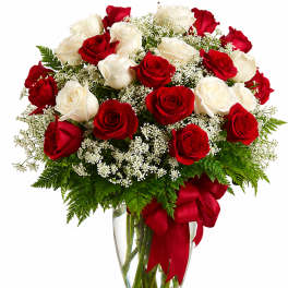 Red and white roses in a clear glass vase with a red ribbon