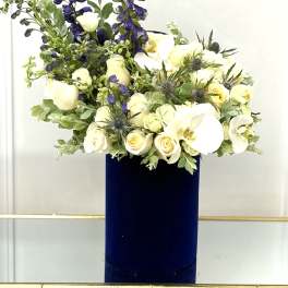 White roses and orchids in a tall navy vase with blue delphinium spikes