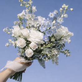Handheld bouquet of white and pale blue flowers against a blue sky