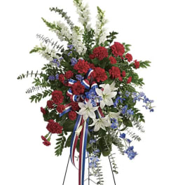 Standing floral spray with red carnations, white lilies, and blue flowers on a tripod stand