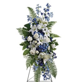 Standing floral spray with white lilies and blue flowers on an easel