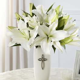White lilies arranged in a tall white vase with a cross emblem