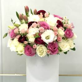 Mixed pink, white, and burgundy flowers arranged in a white box