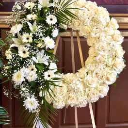 Large white floral wreath on an easel with roses and lilies