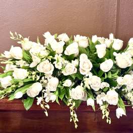 Low arrangement of white roses and orchids on a wooden surface