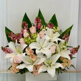 White lilies and pale roses arranged in a box with pink accents