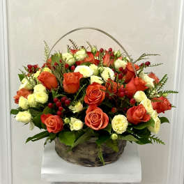 Basket arrangement of orange and white roses with red berries