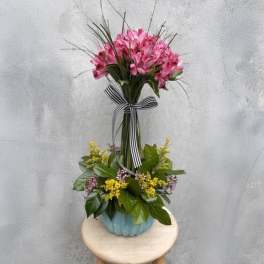Pink flower arrangement in a blue vase with a striped ribbon