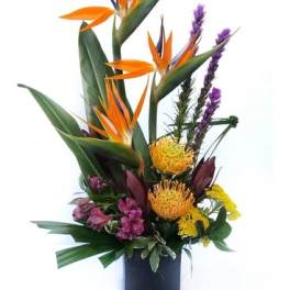 Tall tropical bouquet with orange bird of paradise and purple accents in a dark vase