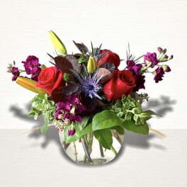 Red roses and purple flowers arranged in a clear glass vase
