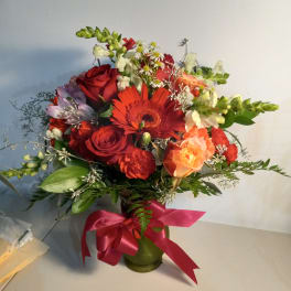 Bouquet of red and peach flowers in a green vase with a pink ribbon