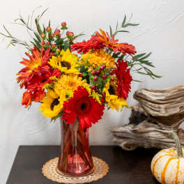 Bright mixed bouquet of sunflowers, gerbera daisies, and mums in a red glass vase